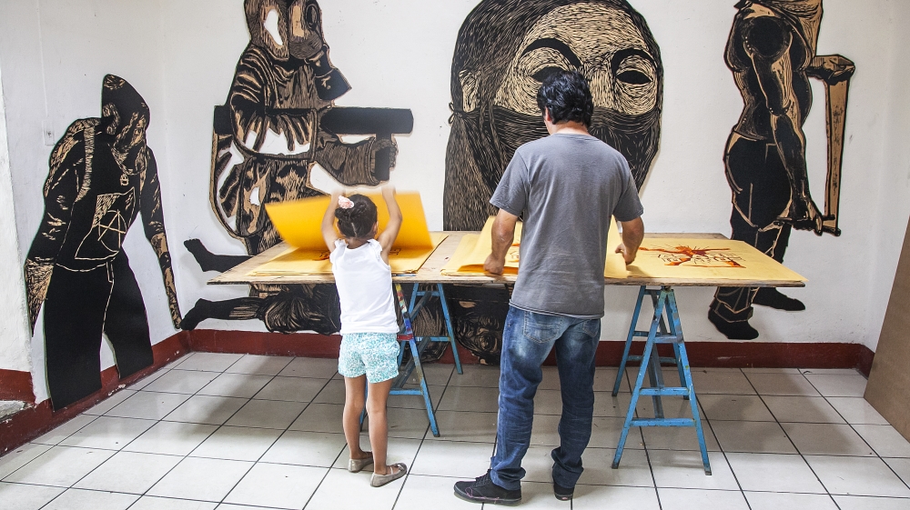 
Mario and his daughter count and sort screen prints for pasting on the city walls. Behind them, large wood prints depict images of protest [Gabriela Campos/XEn News] 
