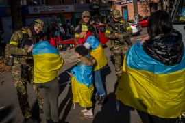 Ukrainians with flags draped around their shoulders ask Ukrainian solider to sign them after the liberation of Kherson