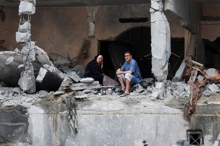 Palestinians sit among the rubble of a damaged residential building, in the aftermath of Israeli strikes, in Gaza City