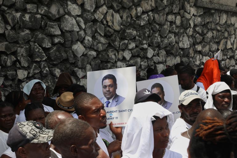 Supporters hold up portraits of Laurent Saint-Cyr outside a stone wall