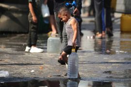 A Palestinian boy carries a large plastic bottle filled with water, after collecting it at a camp for displaced people in the Nuseirat refugee camp, central Gaza Strip, on November 2, 2025 [Eyad Baba/AFP]