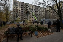 A man sits on a bench as rescuers and others stand near apartment buildings hit during a Russian drone attack, in Dnipro, Ukraine, November 8, 2025 [Mykola Synelnykov/Reuters]
