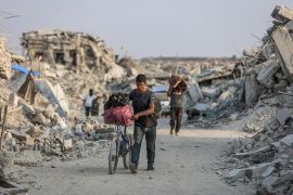 A Palestinian man pushes his bicycle along a road surrounded by the rubble of destroyed buildings in Jabalia, in the northern Gaza Strip [File: AFP]