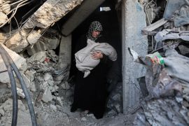 A woman carries a baby in a destroyed building in Jabaliya, northern Gaza [AFP]